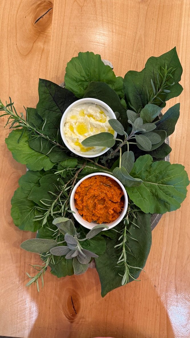 Two dips set on garden leaves, sage, and rosemary